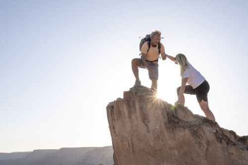 Man reaches down to give woman a hand up, sunbeam shines over mountain peak