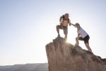 Man reaches down to give woman a hand up, sunbeam shines over mountain peak