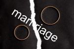 Wedding rings on different halves of a torn sheet of paper. Broken word marriage